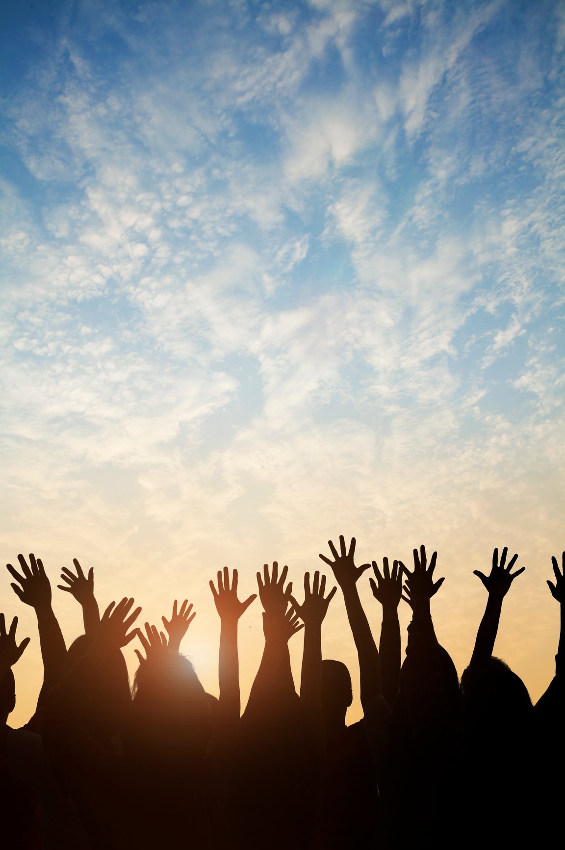 Group of people raising their hands against a sunset